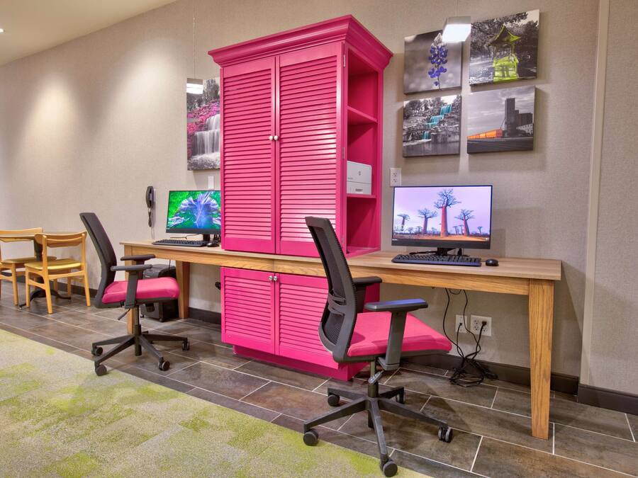 A room with two desks, each with a computer monitor, a keyboard, and a chair. There is a large pink cabinet in the center.