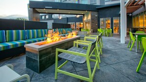 An outdoor seating area with a fire feature, green chairs, and a sofa with striped cushions. - Home2 Suites by Hilton Wichita Falls, TX (Wichita Falls)