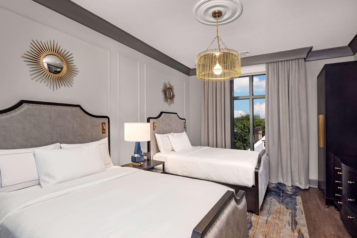 A hotel room with two beds, a chandelier, a large mirror, and a view of the outdoors.
