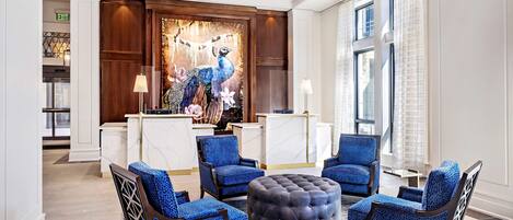 Una hall con quattro poltrone blu, un pouf rotondo, una scrivania della reception e un murale con un pavone.