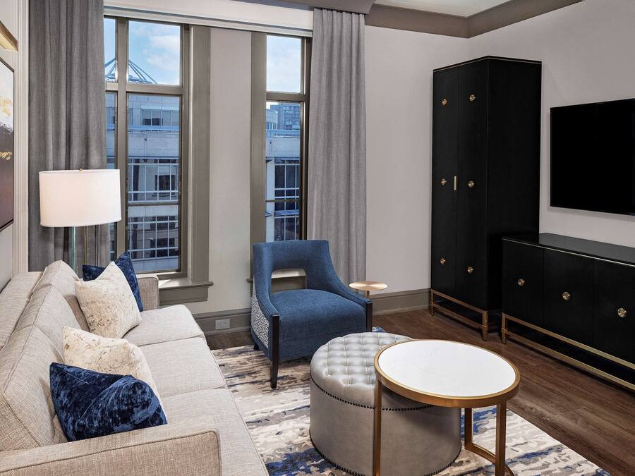 A modern living room with a sofa, ottoman, armchair, and a TV mounted on the wall.
