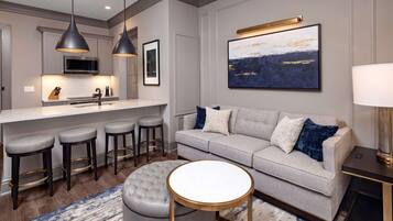 A modern kitchen with a central island, bar stools, a tufted ottoman, and a round coffee table.