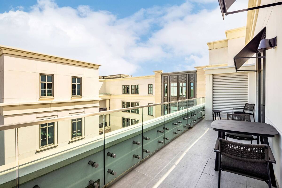 A balcony with a glass railing, a table, and chairs.