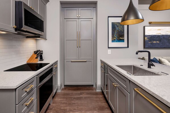 A modern kitchen with grey cabinetry, a built-in microwave, a double sink, and a wooden cutting board. - Hilton Club Liberty Place Charleston (Charleston)