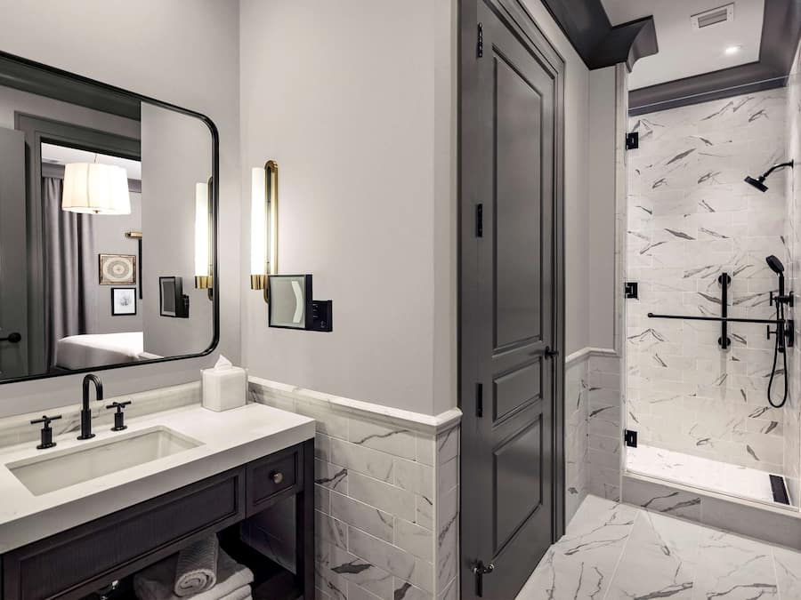 Une salle de bain moderne avec un grand miroir, un lavabo, un porte-serviettes et un espace douche doté d'un pare-douche en carreaux de marbre.