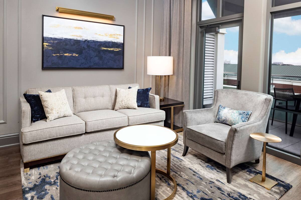 A modern living room with a sofa, armchair, ottoman, and round coffee table.