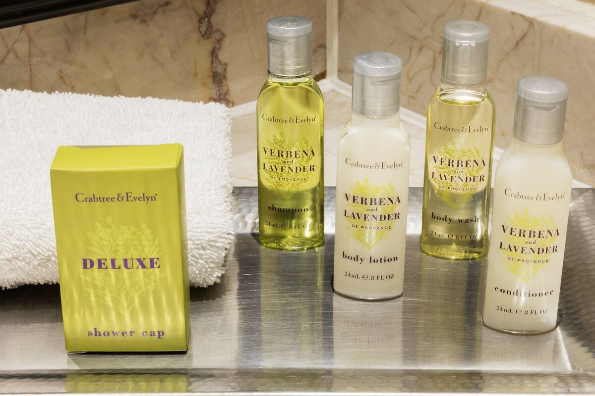A bathroom shelf with various Crabtree & Evelyn products including a shower cap, body lotion, and conditioner.
