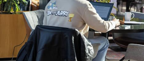 Eine Person sitzt an einem Tisch im Freien mit einem Laptop, umgeben von Blumentöpfen und einem Kicker.