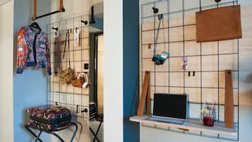 Una habitación con pared azul, un panel de pared de madera, una computadora portátil sobre una repisa, una maleta y un bolso estampado de leopardo.