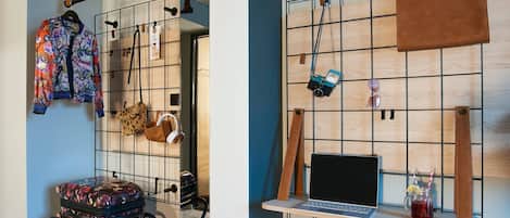 A room with a blue wall, a wooden grid wall, a laptop on a shelf, a suitcase, and a leopard print bag.