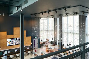Eine moderne Hotelhalle mit einem großen Fernsehbildschirm, Sitzbereichen und großen Fenstern mit Tageslicht.