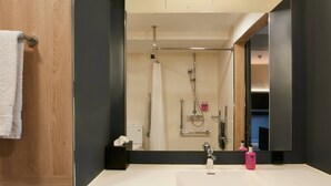A modern bathroom with a large mirror, white sink, and a shower area.