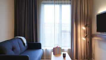 A room with a sofa, a table with a gift bag and a cup, a floor lamp, and a TV on the wall.