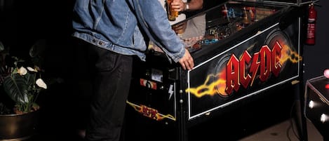 Un uomo in piedi davanti a un cabinato arcade, con un drink in mano.