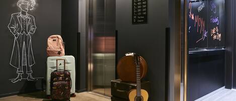 An elevator with a neon sign listing floor numbers and a neon sign with phrases like "Moxy" and "Fabulous."