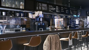 A modern bar area with a menu board, stools, and a city view through the window.
