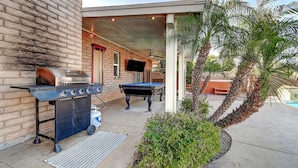 An outdoor patio with a barbecue grill, pool table, and palm trees.