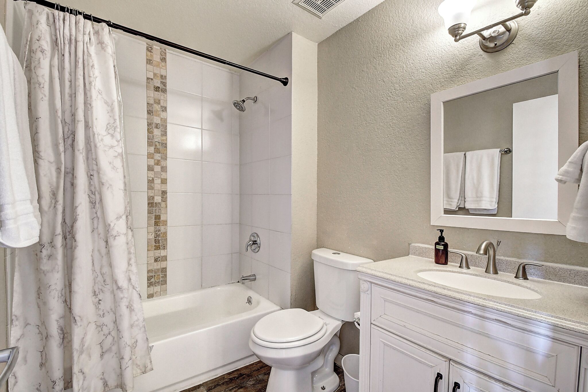 A bathroom with a bathtub, toilet, sink, and a mirror with a towel hanging on it.