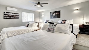 A hotel room with two beds, a ceiling fan, an air conditioner, a sign for a theater and lounge, and a window with blinds.