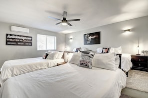 A hotel room with two beds, a ceiling fan, an air conditioner, a sign for a theater and lounge, and a window with blinds.