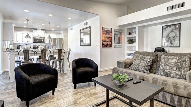 A modern living room with a sofa, armchairs, and a coffee table. There is a kitchen in the background with a dining area.
