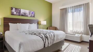 A hotel room with a large bed, a nightstand, a chair, a desk, a lamp, and a window with curtains.