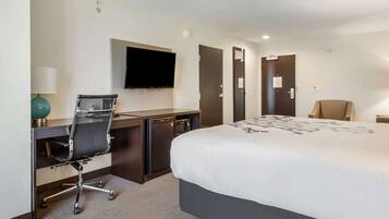 Quarto de hotel com cama, escrivaninha, cadeira, televisão e uma pequena cozinha.