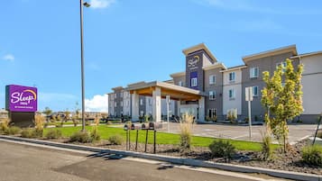 A Sleep Inn by Choice Hotels building with a modern design, a parking lot, and a well-maintained lawn area.