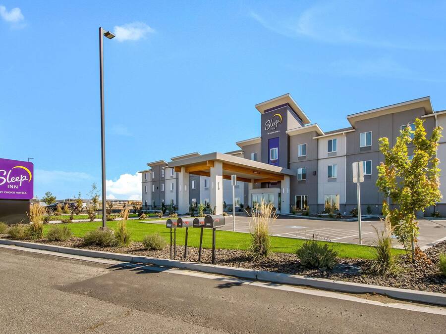 A Sleep Inn by Choice Hotels building with a modern design, a parking lot, and a well-maintained lawn area.