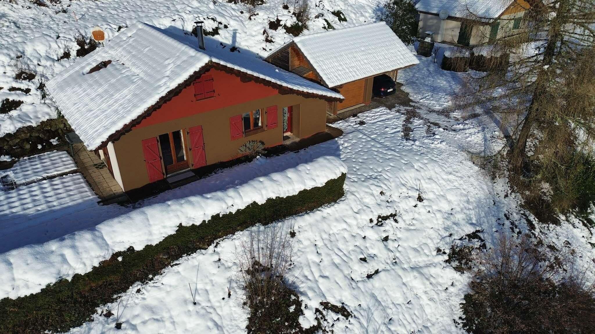 Een chalet met twee verdiepingen, met een rode gevel en sneeuwbedekte daken, gelegen in een besneeuwd landschap.