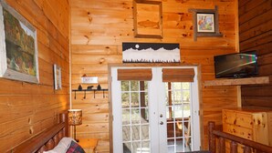 A wooden cabin bedroom with a bed, a television, and a door leading outside. - King's River Cabin-River Frontage - Fire Pit - Screened Porch (Bryson City)