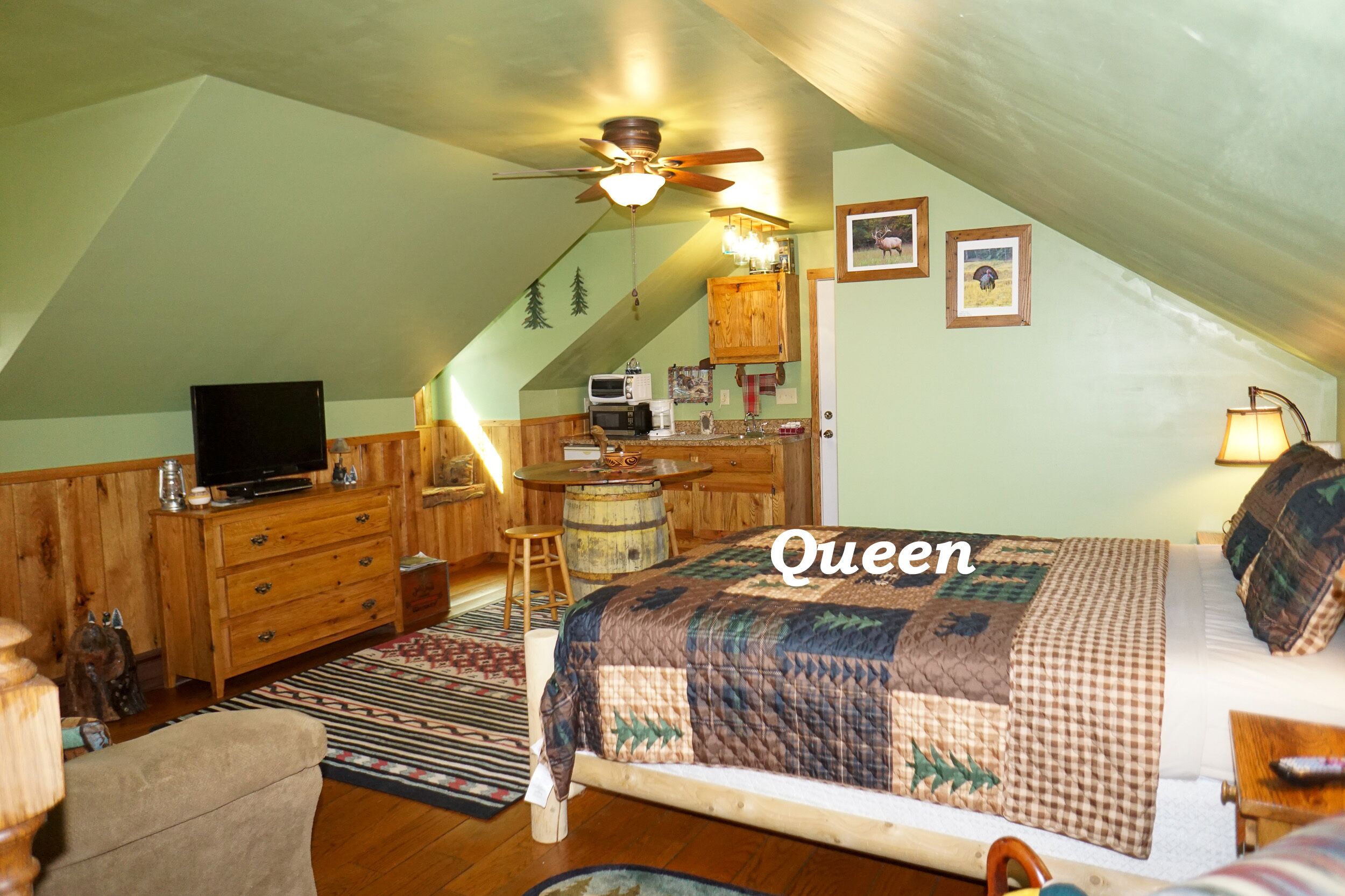 A cozy attic bedroom with a queen-sized bed, wooden furniture, a ceiling fan, and a television.