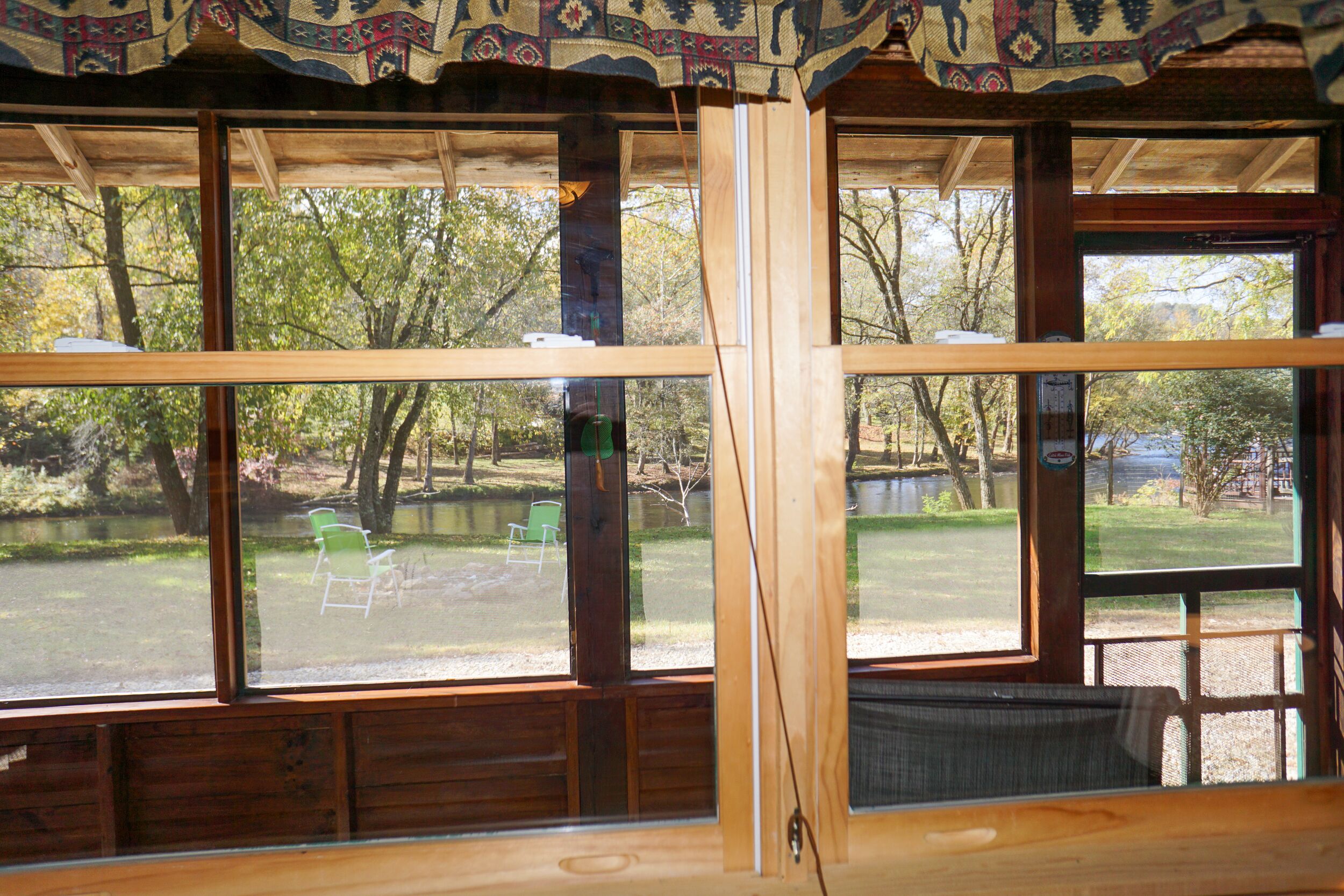 A room with large windows, wooden beams, and a view of an outdoor area with chairs and trees.