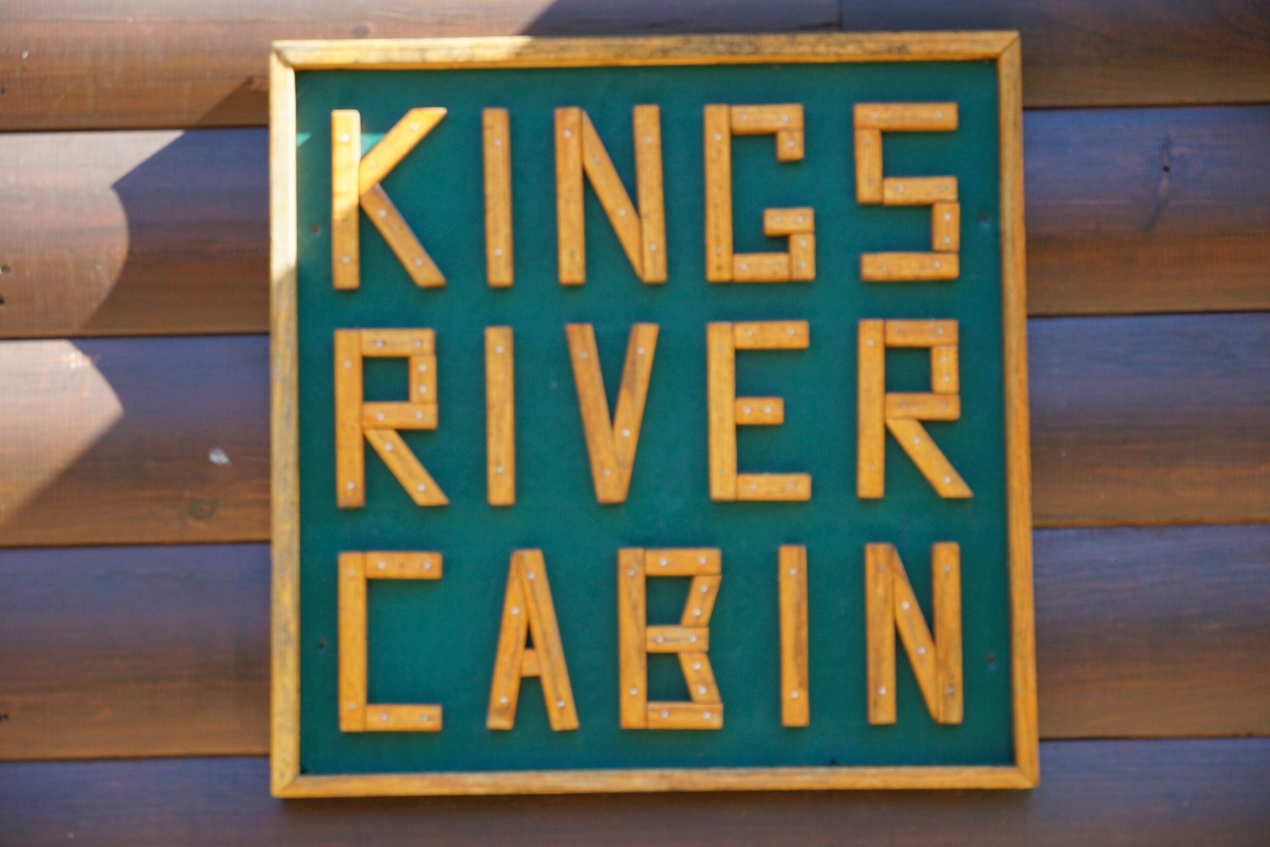 Ein hölzernes Schild mit dem Aufdruck 'KINGS RIVER CABIN', an einer Holzwand befestigt.