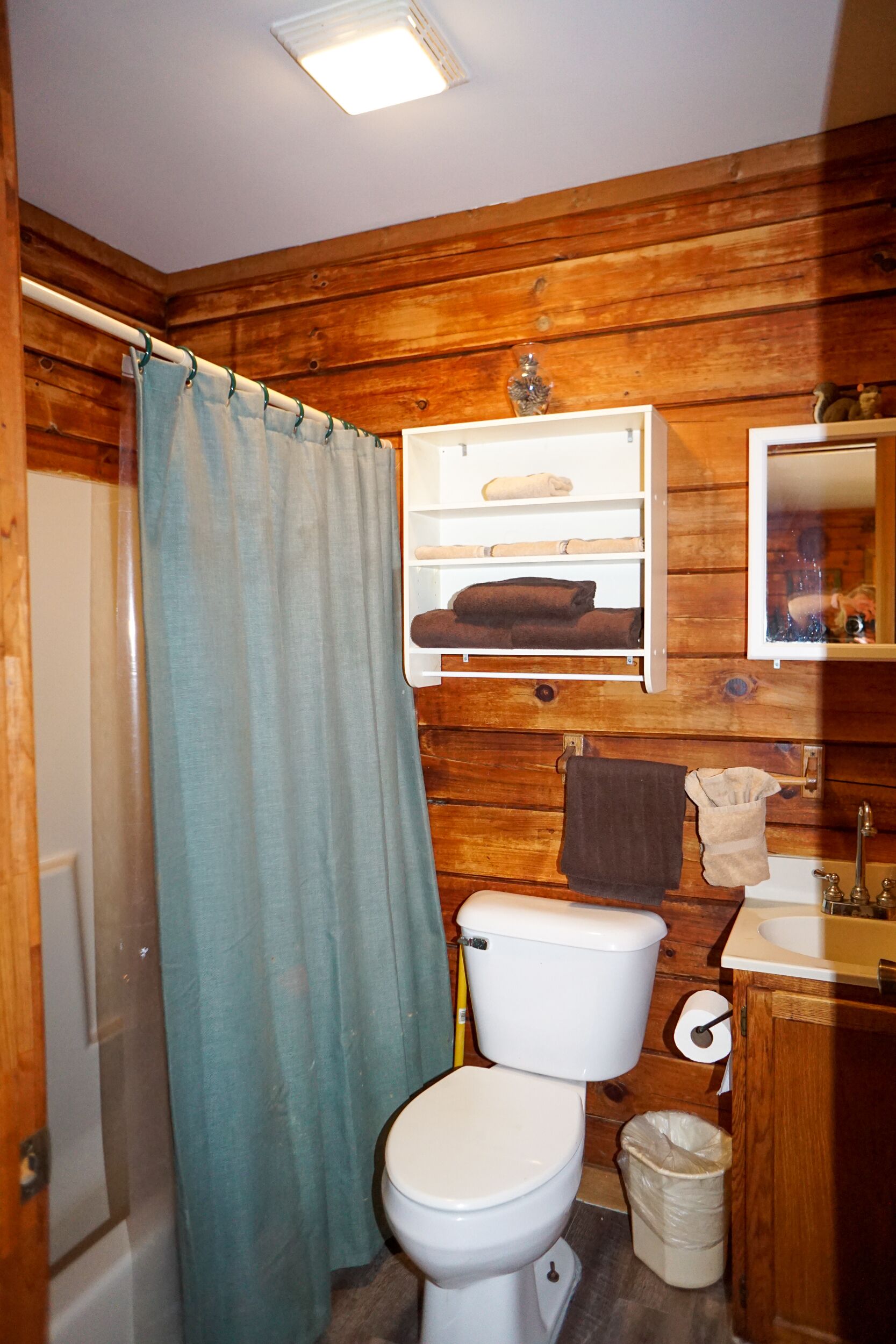 A wooden-paneled bathroom with a toilet, sink, and a shelf with towels.