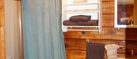 A wooden-paneled bathroom with a toilet, sink, and a shelf with towels.