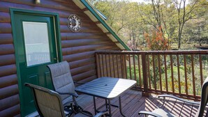 A wooden deck with a table and chairs, a green door, and a window with a grid pattern. - King's River Cabin-River Frontage - Fire Pit - Screened Porch (Bryson City)