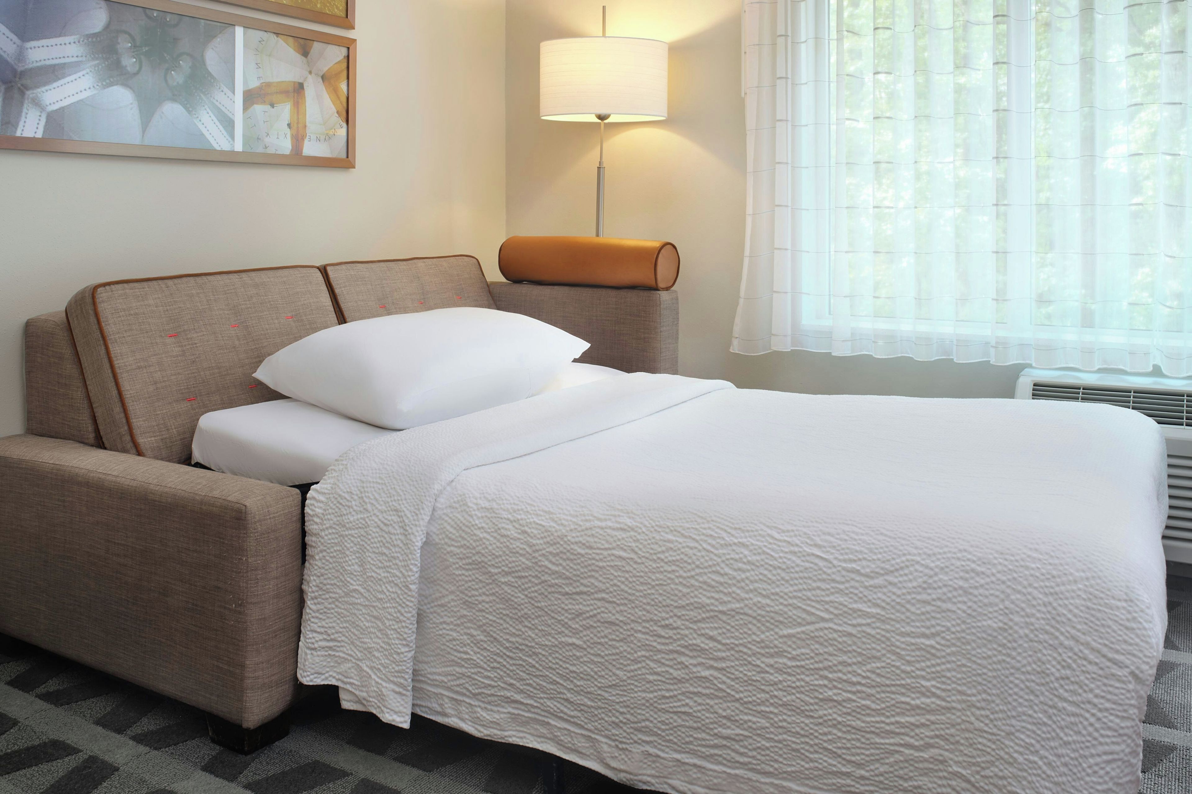 A hotel room with a bed, a nightstand, a lamp, and a window with curtains.