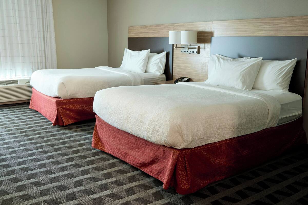 Habitación de hotel con dos camas, alfombra estampada y una lámpara de pared.