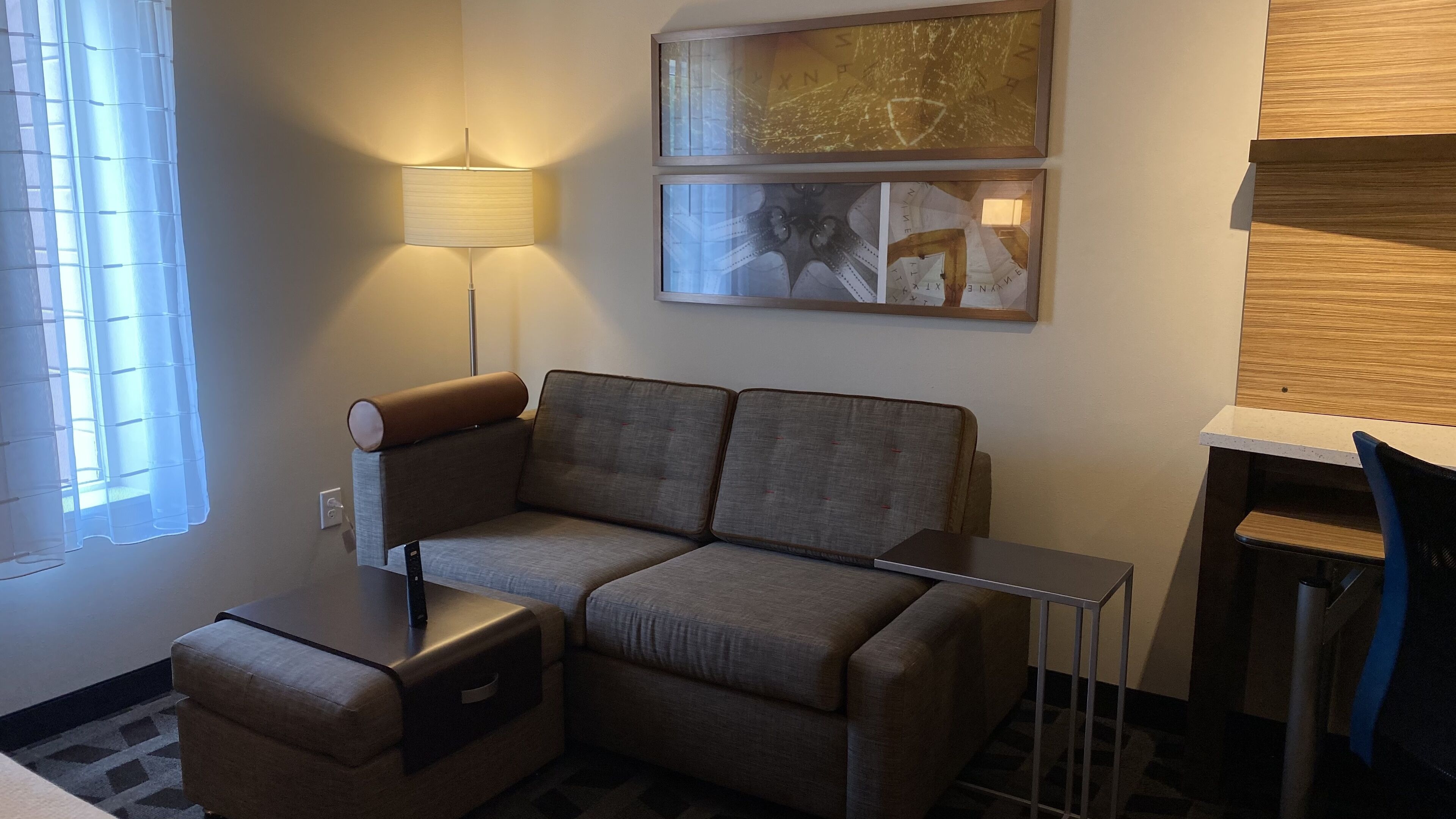 Un salon moderne avec un canapé, une petite table, une lampe et une fenêtre équipée de stores.