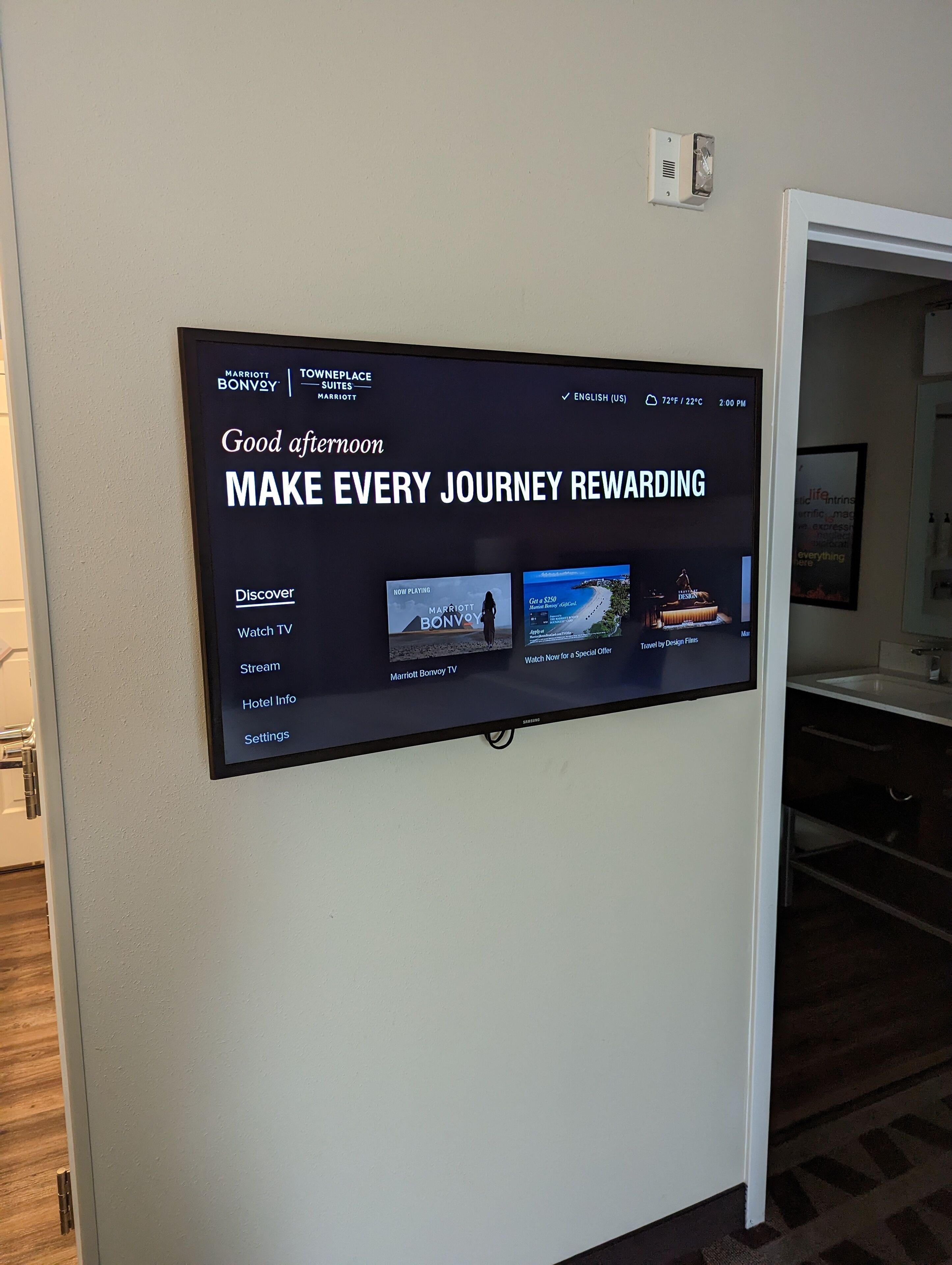 A digital display in a hotel lobby advertising Marriott Bonvoy's TV service, with options to watch TV, stream content, access hotel info, and adjust settings.