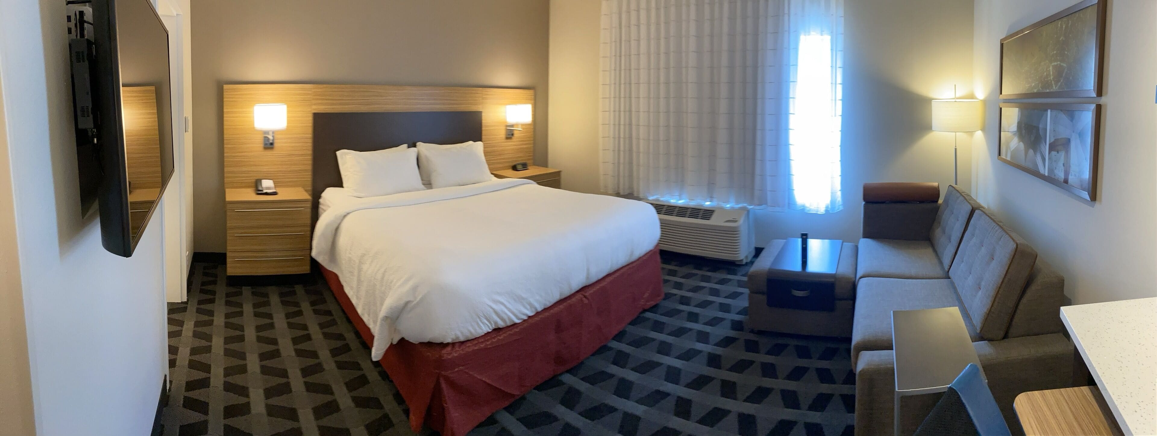 A hotel room with a large bed, bedside tables, a desk, a chair, and a window with curtains.