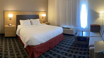 A hotel room with a large bed, bedside tables, a desk, a chair, and a window with curtains.