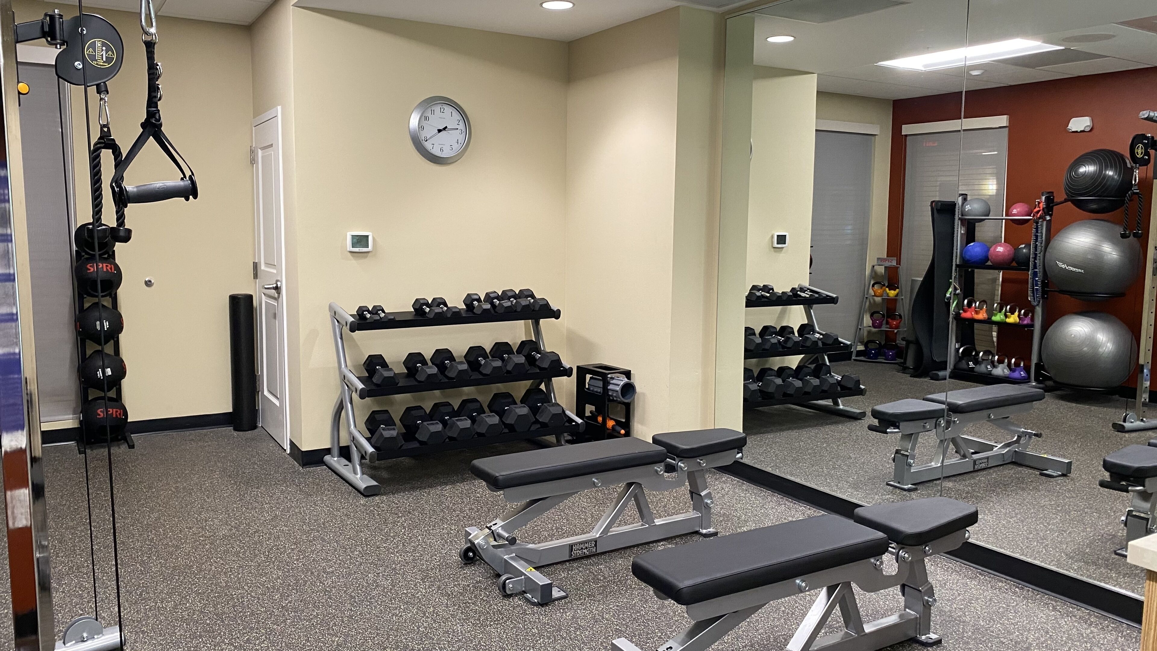 A gym with multiple benches, dumbbells, and exercise balls.