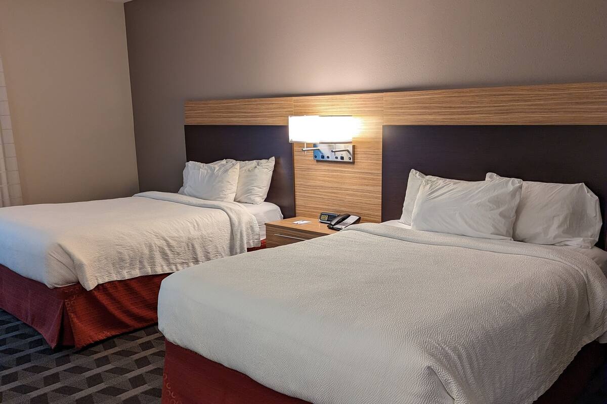 Habitación de hotel con dos camas, una mesita de noche con un teléfono y una lámpara de pared.