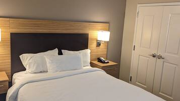 A neatly made bed with white linens, a wooden headboard, and a bedside lamp.