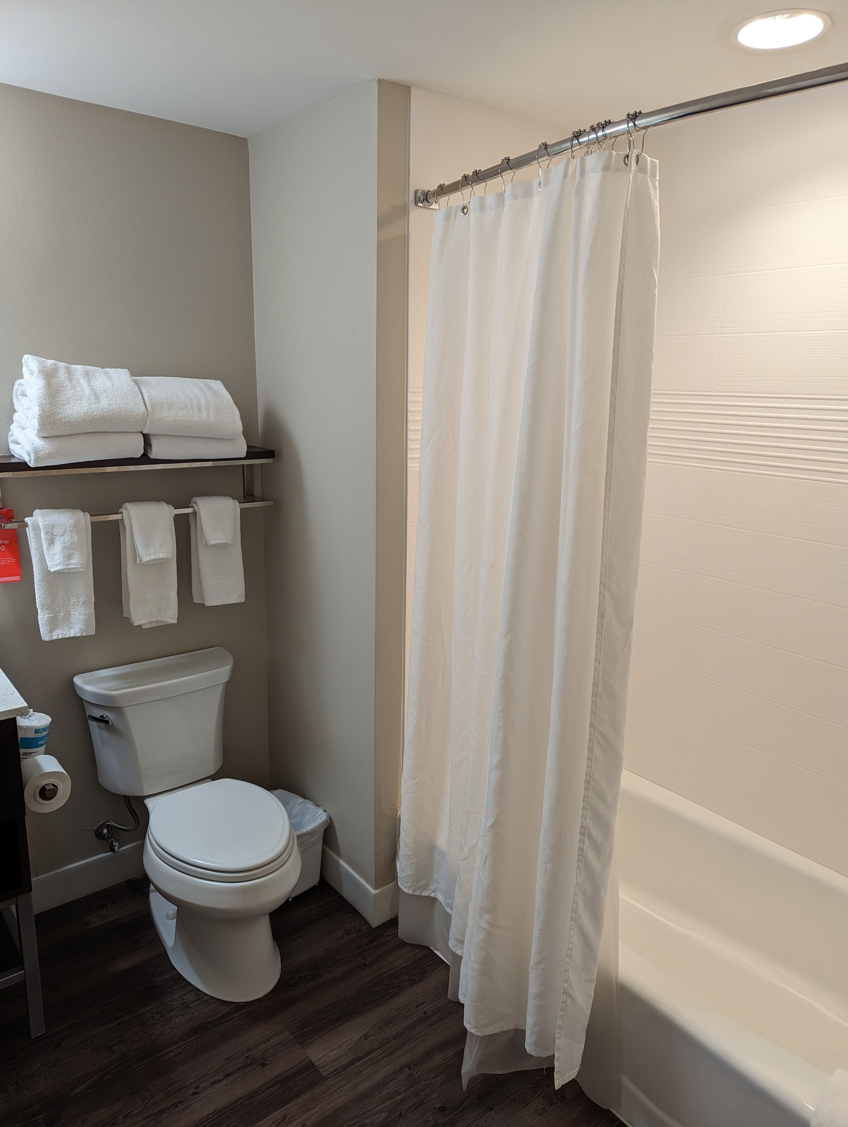 A bathroom with a toilet, a shelf with folded towels, and a shower curtain.
