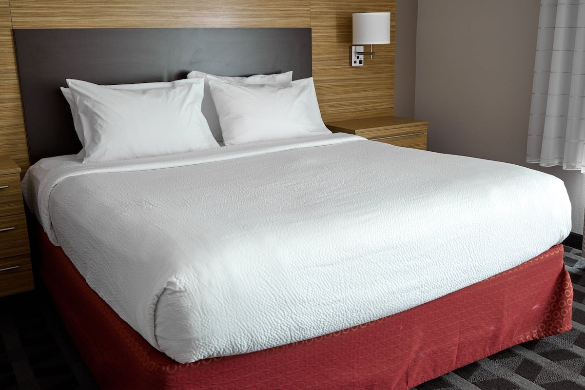 Habitación de hotel con una cama grande, cabecero de madera, mesitas de noche y una lámpara de pared.