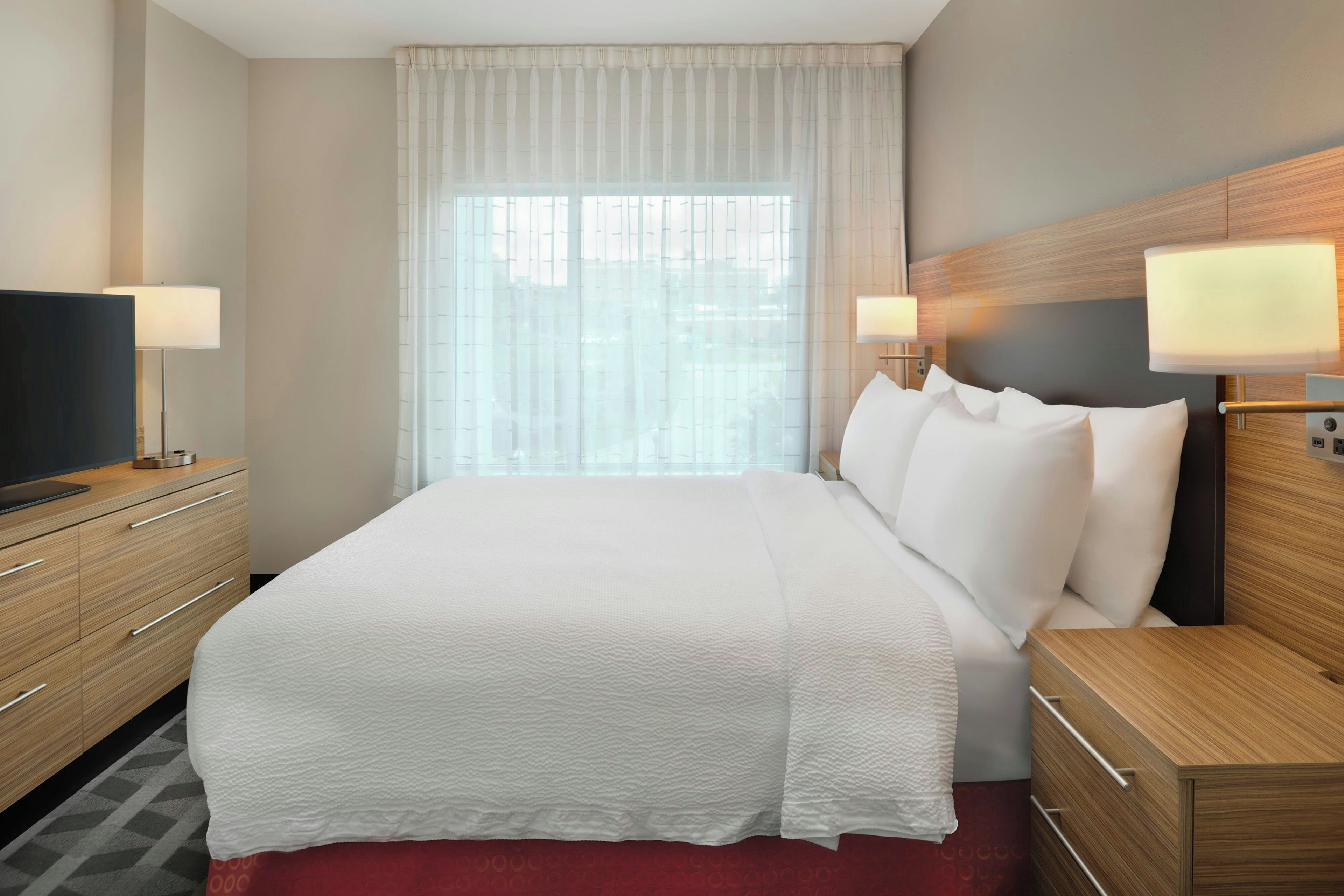 A hotel room with a large bed, a television on a wooden dresser, and two bedside lamps.
