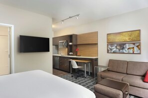 Una habitación de hotel moderna con cama, kitchenette, zona de estar y obras de arte en la pared.